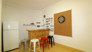 A compact kitchen with a refrigerator, a wooden counter, and a dartboard on the wall.