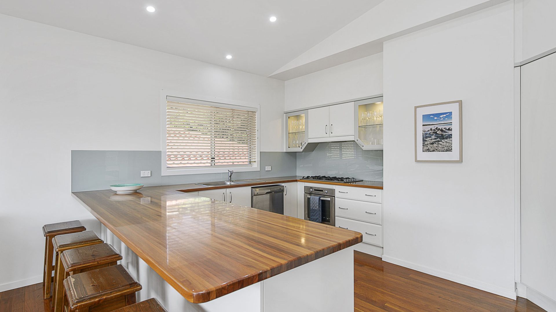 A modern kitchen with a wooden island, white cabinetry, and a window with blinds.