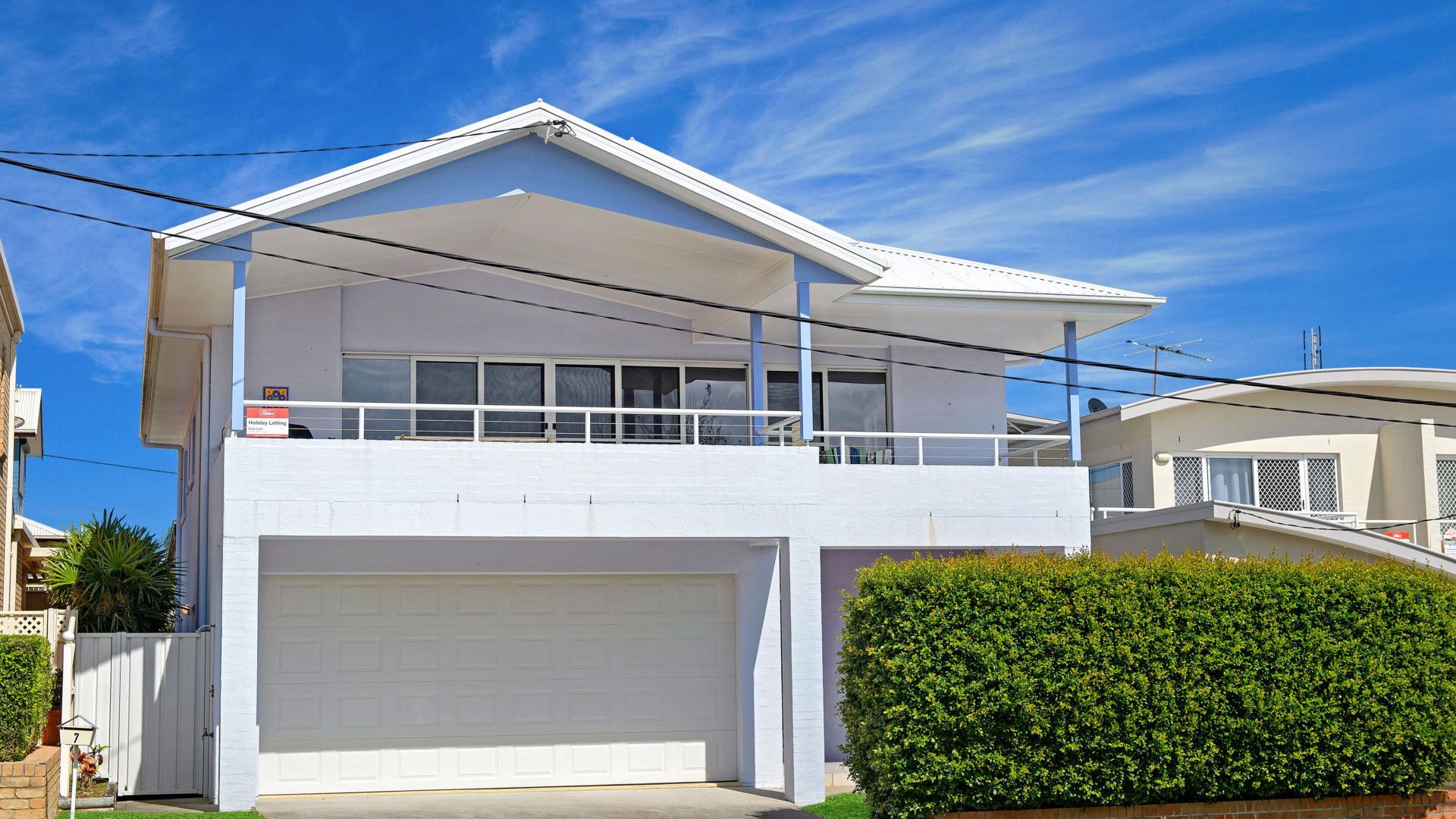 A two-story house with a garage, a balcony, and a well-maintained hedge.