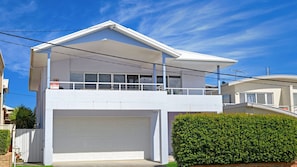 A two-story house with a garage, a balcony, and a well-maintained hedge.