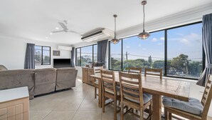 A modern living room with a sofa, dining table, chairs, and a TV. - Bombora, 3/4 East Street (Crescent Head)