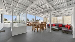 A covered outdoor area with a dining table and chairs, a sofa with cushions, and a view of the outdoors.