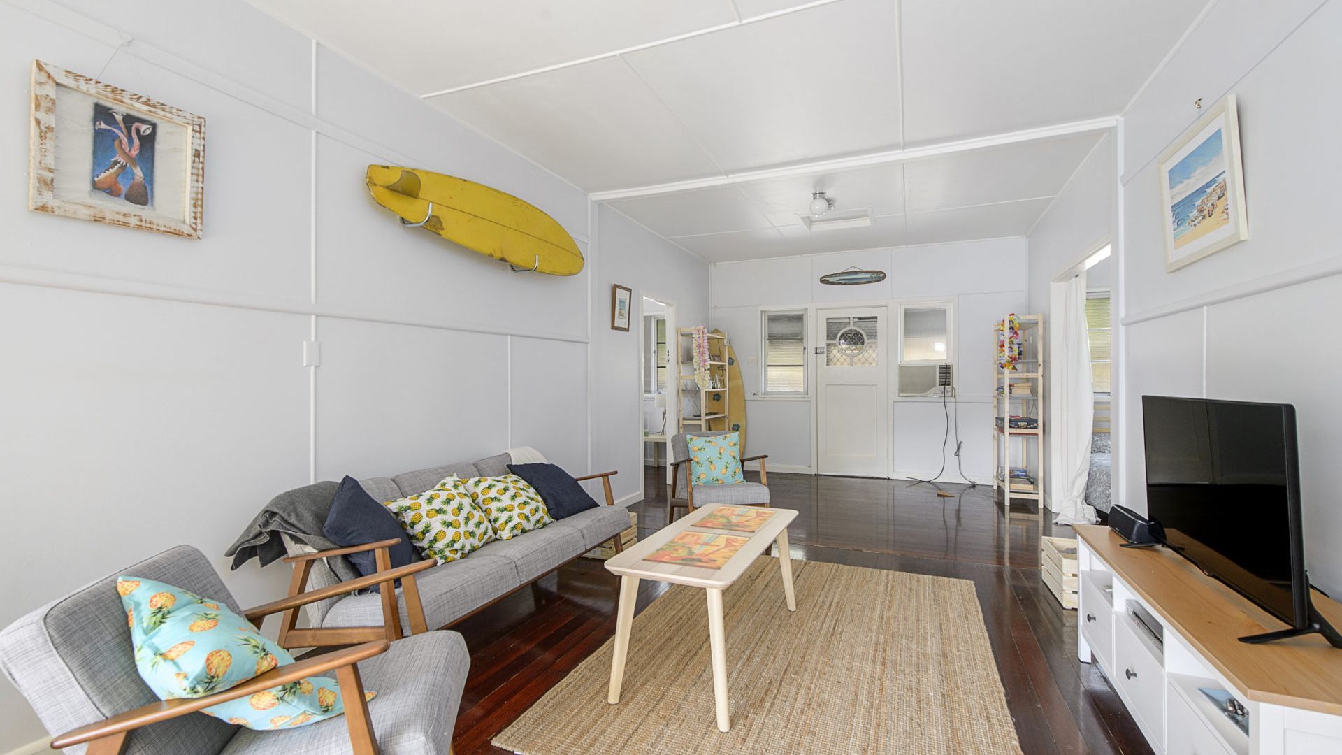 Un salon comprenant un canapé, des fauteuils, une table basse, un téléviseur et une planche de surf accrochée au mur.