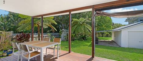 A covered patio with a table and chairs, surrounded by a lush garden and a white garage.