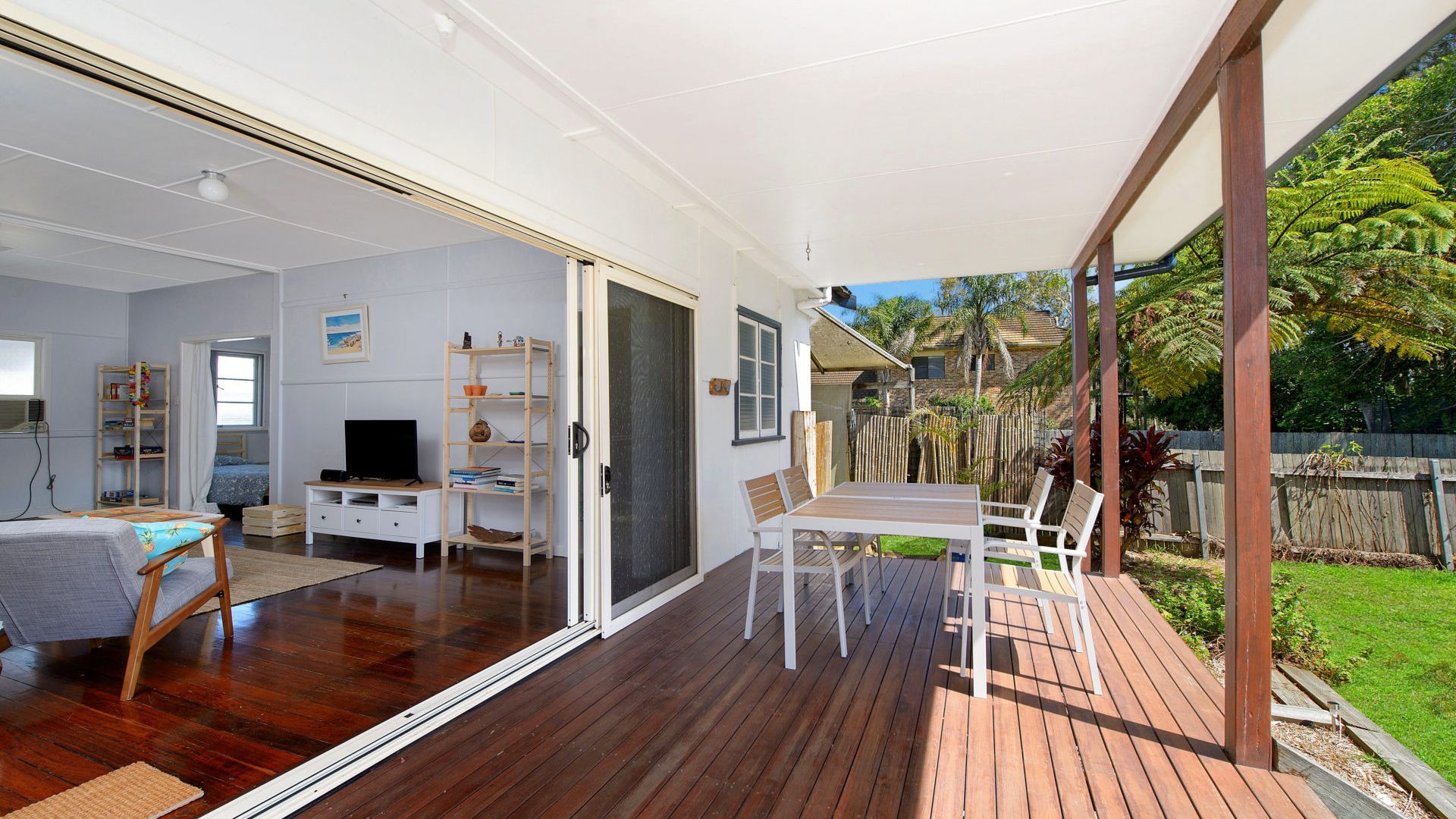 A spacious living area with a sliding glass door leading to a deck, a television, a bookshelf, and a dining table with chairs.