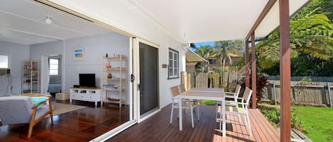 A spacious living area with a sliding glass door leading to a deck, a television, a bookshelf, and a dining table with chairs.