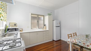 A compact kitchen with a gas stove, a refrigerator, and a window with blinds.
