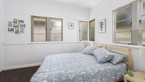 Een slaapkamer met een bed, een nachtkastje en een raam met jaloezieën.