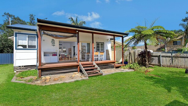 Een gelijkvloers huis met een overdekte veranda, een zichtbare keuken en een omheinde achtertuin.