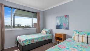 A bedroom with two single beds, a wooden nightstand, a window with curtains, and a painting on the wall.