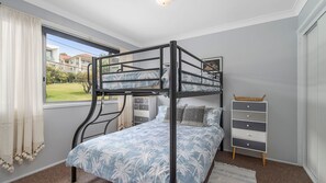 Een slaapkamer met stapelbedden en uitzicht op een tuin en huizen.