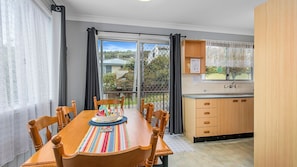 A dining area with a wooden table and chairs, a kitchen with wooden cabinets, and a view through a glass door.