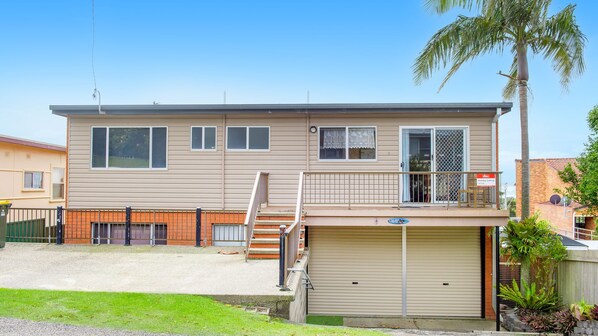 A two-story residential building with a garage, a balcony, and a palm tree.