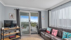 A living room with a television, a sofa with colorful cushions, a bookshelf, and a sliding glass door leading to a balcony.