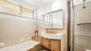 A modern bathroom with a bathtub, a sink with a mirror above it, and a shower area. - Beachcomber, 27 Dulconghi Street (Crescent Head)