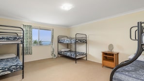 A room with bunk beds, a window with curtains, a small wooden cabinet, and a mirror.