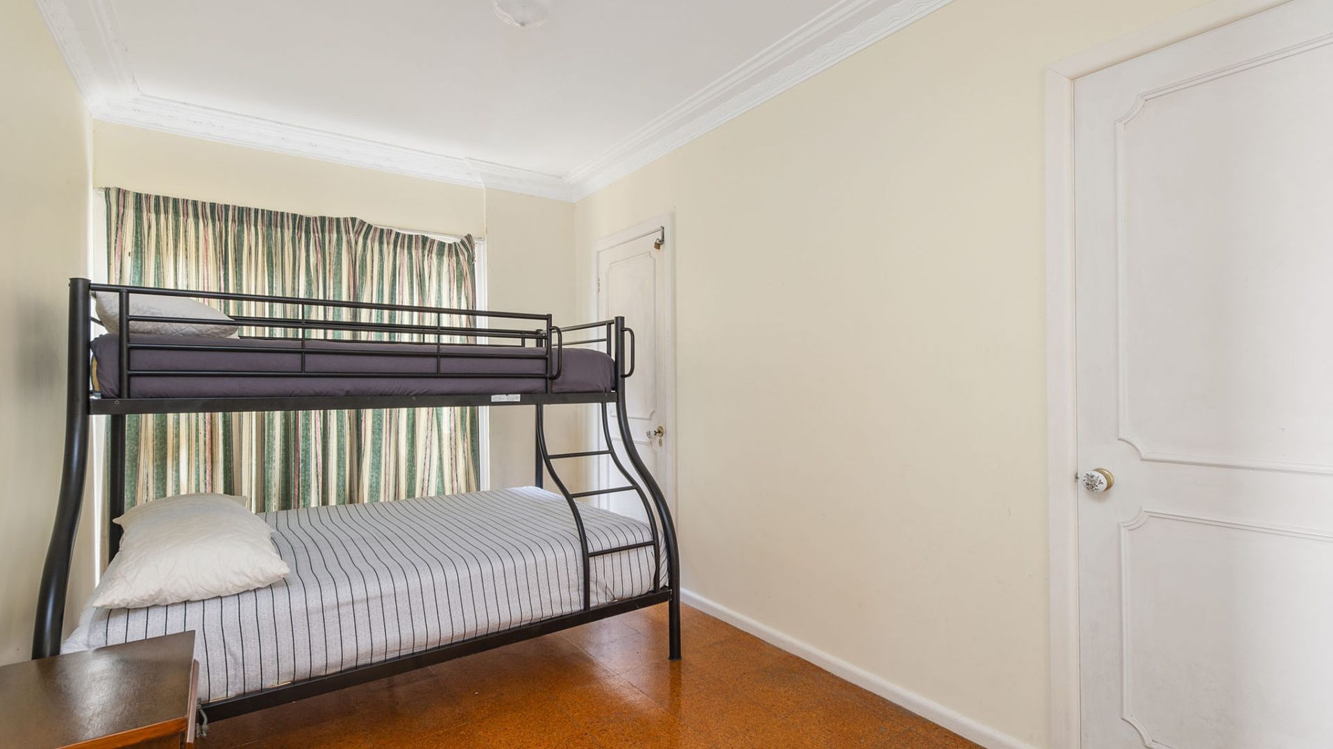 A bunk bed in a room with a door and a window with curtains.