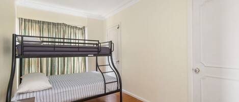 A bunk bed in a room with a door and a window with curtains.