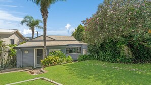 A single-story house with a small front yard, a palm tree, and a flowering bush.