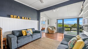 A modern living room with a grey sofa, a wicker chair, and a view of the outdoors. - Sea Salt, 24 Stewart Street (Crescent Head)