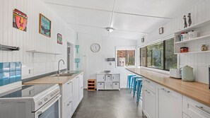 A kitchen with white cabinetry, a wooden countertop, a sink, a stove, and a window with a view of greenery.