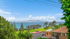 A residential area with a view of the sea, a mountain in the distance, and a house with a red roof. - Sea Salt, 24 Stewart Street (Crescent Head)
