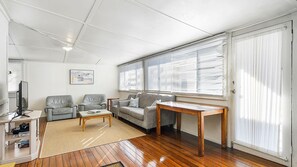 A living room with a sofa, armchairs, a coffee table, a TV, and a large window with blinds.