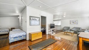 Quarto moderno e bem iluminado, com piso de madeira, sofá, mesa de centro, rack para TV e cama com roupa de cama estampada.