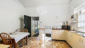 A compact kitchen with a dining area, featuring a stove, microwave, and a clock on the wall.