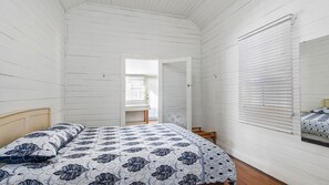 Ein Schlafzimmer mit einem Bett, einem hölzernen Kopfteil, einem Fenster mit Jalousien und einer Tür zu einem anderen Raum.