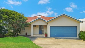 Une maison à deux étages, avec un toit recouvert de tuiles rouges, une porte de garage bleue et une pelouse bien entretenue.
