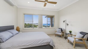 A bedroom with a large bed, two chairs, a floor lamp, and a view of the ocean.