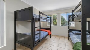Une chambre de dortoir avec des lits superposés, une fenêtre donnant sur les arbres et un sol carrelé.