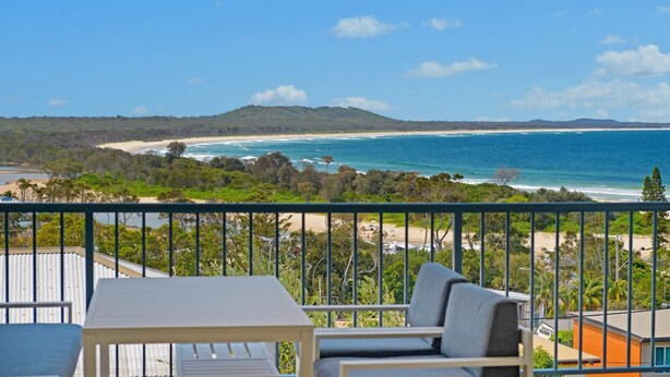 Un balcon avec une table et des chaises donnant sur une plage et l’océan.