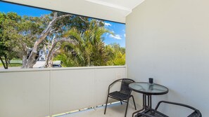 A balcony with a view of trees and a parked car, a round table, and two chairs. - Maliblue, 5/1 Main Street, Crescent Head (Crescent Head)