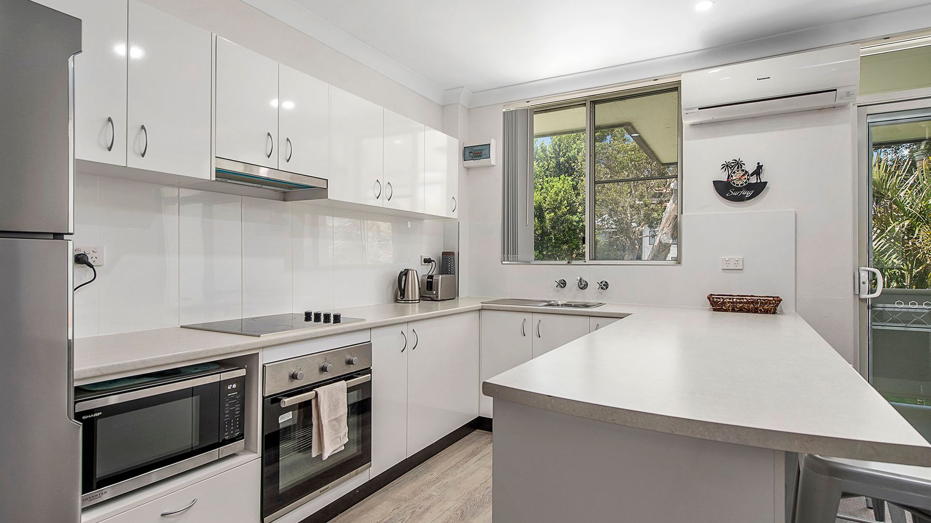 A modern kitchen with white cabinetry, a built-in oven, a stovetop, and a large window offering a view of greenery.