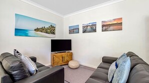 A living room with a flat-screen TV, two leather sofas, a wooden cabinet, and four framed pictures on the wall.