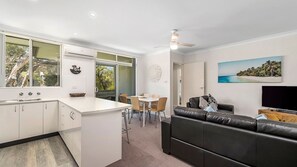 A modern kitchen with a dining area, a living room with a sofa, and a TV. - Maliblue, 5/1 Main Street, Crescent Head (Crescent Head)