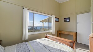 Ein Schlafzimmer mit Bett, Schreibtisch, Fenster mit Blick und Tür.