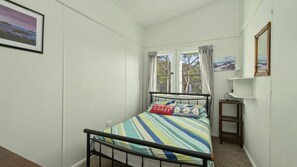A bedroom with a bed, a window, a bedside table, and a wall-mounted shelf.