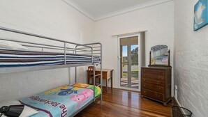 Une chambre avec un lit superposé, un bureau et une commode, une porte-fenêtre coulissante donnant sur un espace extérieur, et un tableau encadré au mur.