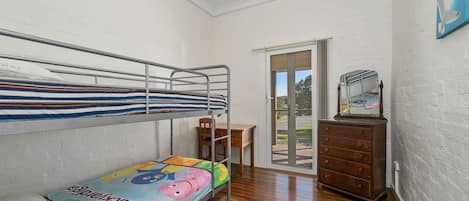 A bunk bed room with a desk and dresser, a sliding glass door to an outdoor area, and a framed picture on the wall.