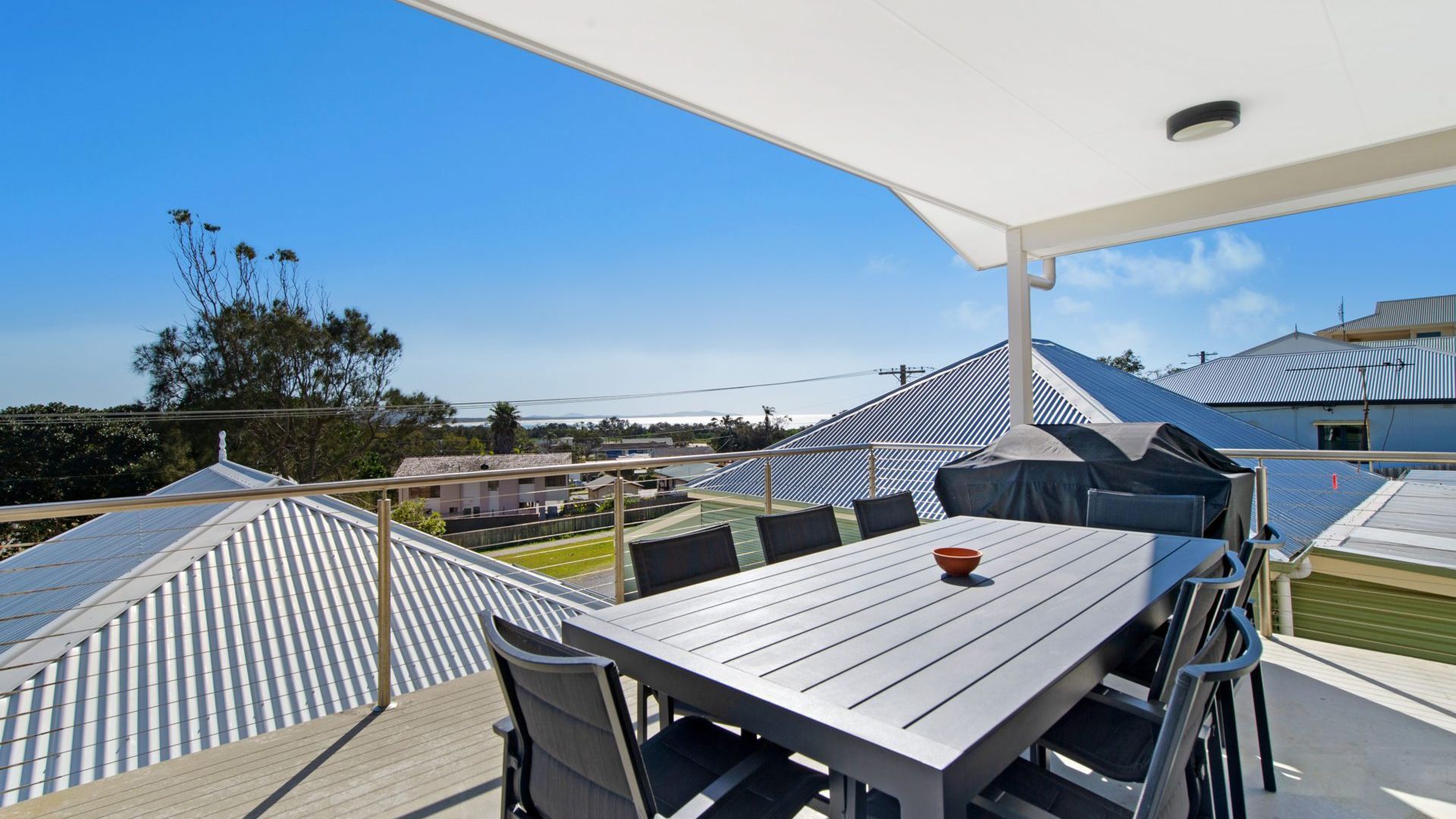 An outdoor patio with a table and chairs, a covered seating area, and a view of buildings and trees.