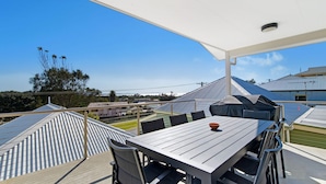 Une terrasse extérieure avec une table et des chaises, un espace salon couvert et une vue sur les bâtiments et les arbres.