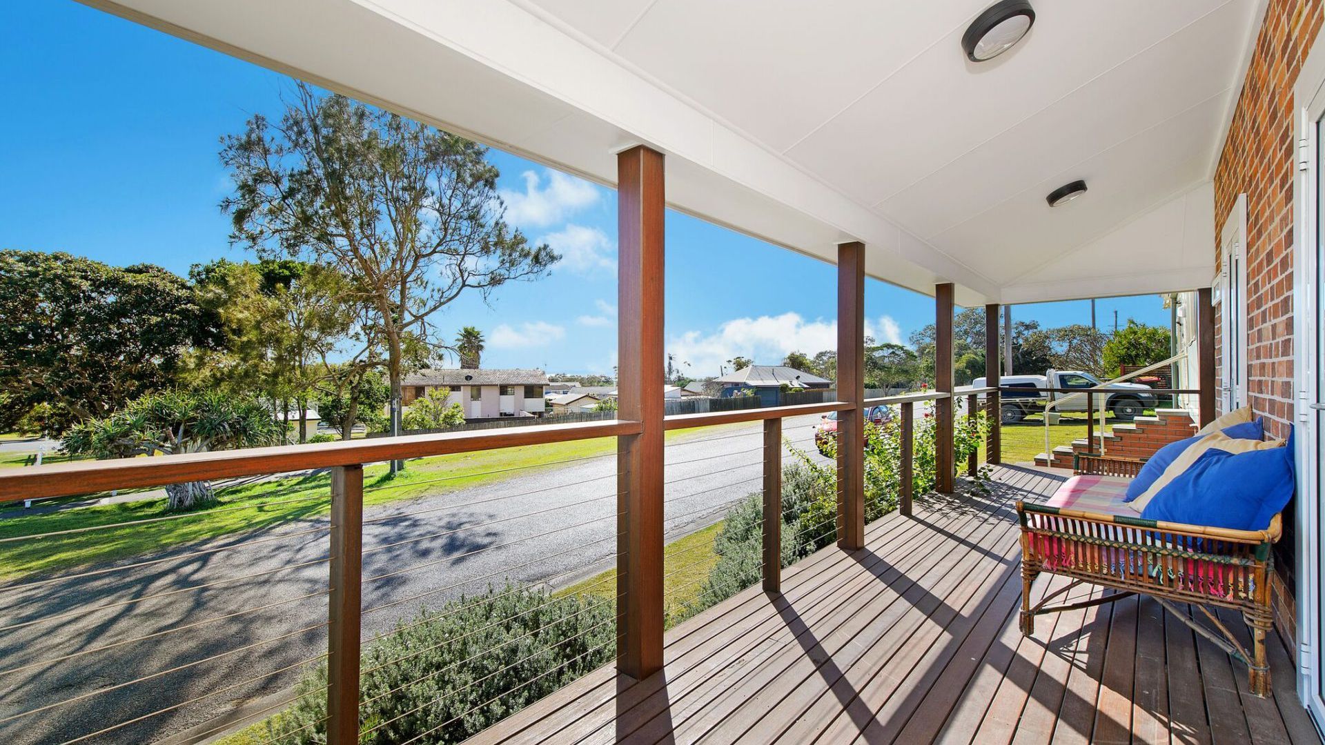 A wooden deck with a railing, a lounge chair, and a view of a road and buildings.