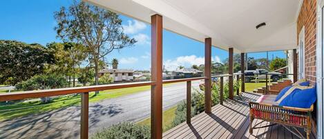 A wooden deck with a railing, a lounge chair, and a view of a road and buildings.