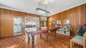 A room with a wooden floor, a dining table, a kitchen area, and a bookshelf with books and golf equipment.