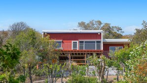 Un edificio rojo de dos pisos con un balcón, rodeado de árboles y vegetación.