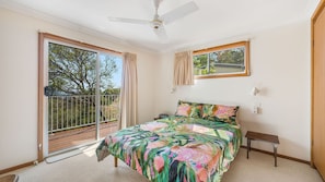 A bedroom with a bed, a ceiling fan, a window, and a balcony.