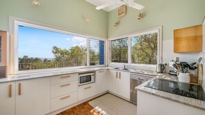 A modern kitchen with white cabinetry, a built-in microwave, and a large window offering a view of trees and the sky.